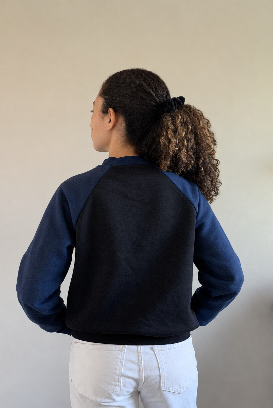 Vista traseira da modelo com camisola azul-marinho e preta, cabelo retocado naturalmente